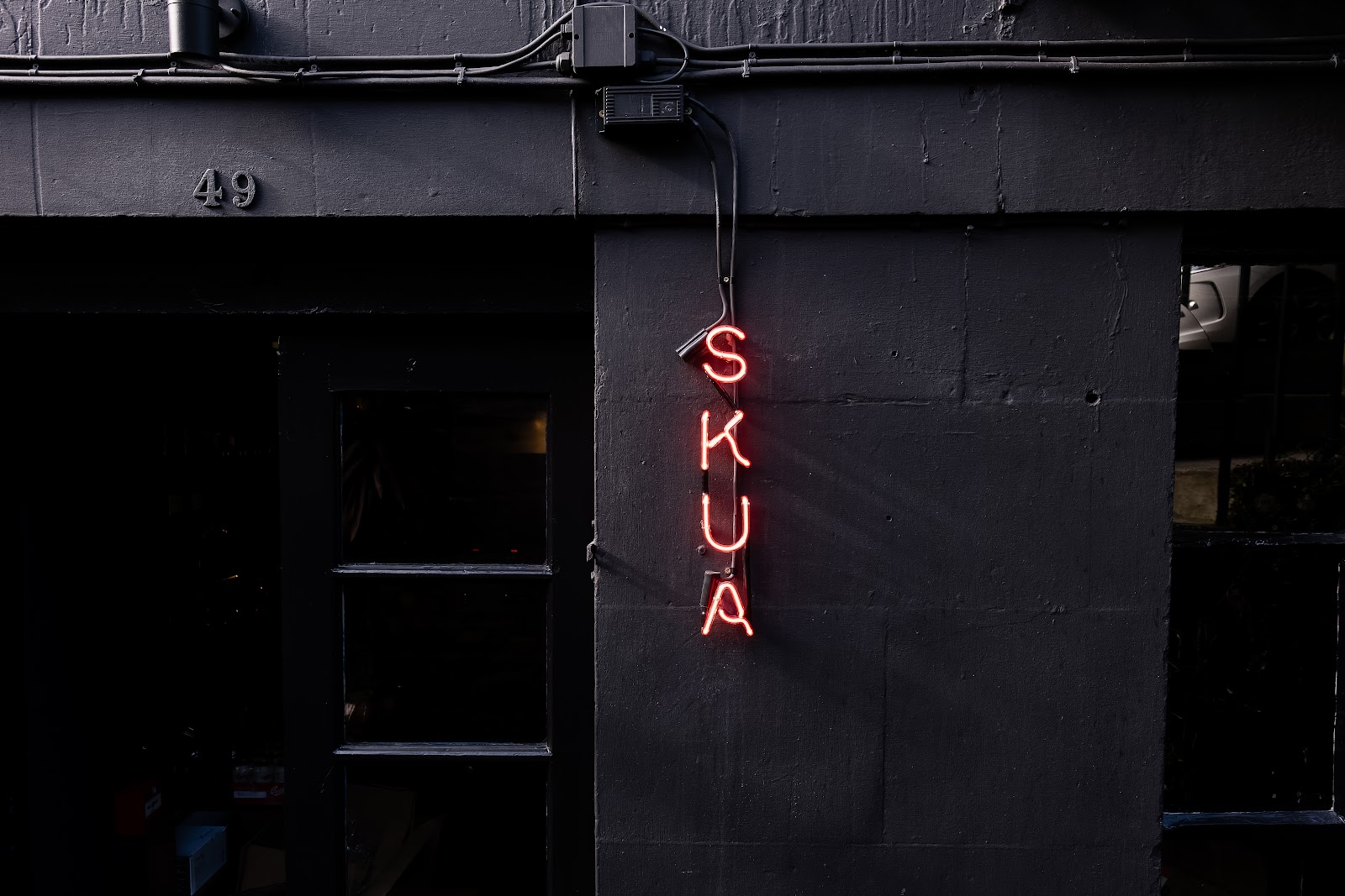 The dark front of Skua at 49 St Stephen Street in Stockbridge, with its name in red neon letters down the wall beside the door.