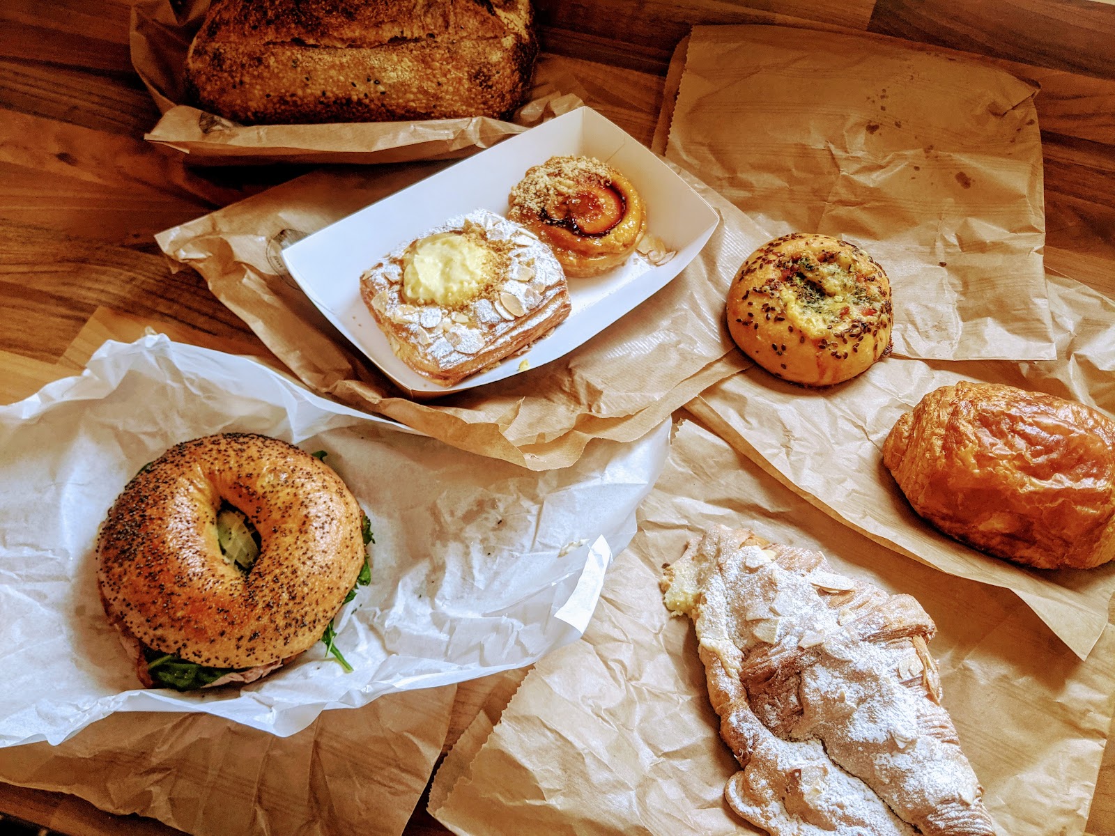Bakes from Big Bear Bakery laid out on paper: a filled bagel, an almond croissant, danishes and a loaf of sourdough.