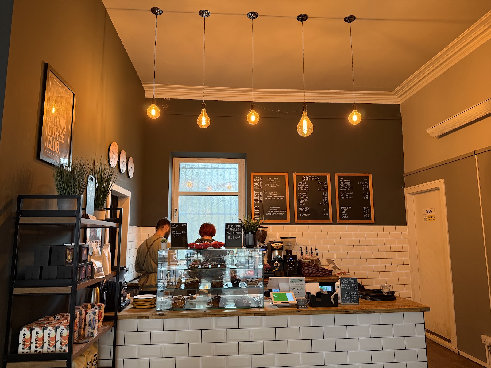 The counter at Fearless Coffee on Rosemount Place, with cakes under glass, coffee menus on the wall and bulbs hanging overhead.