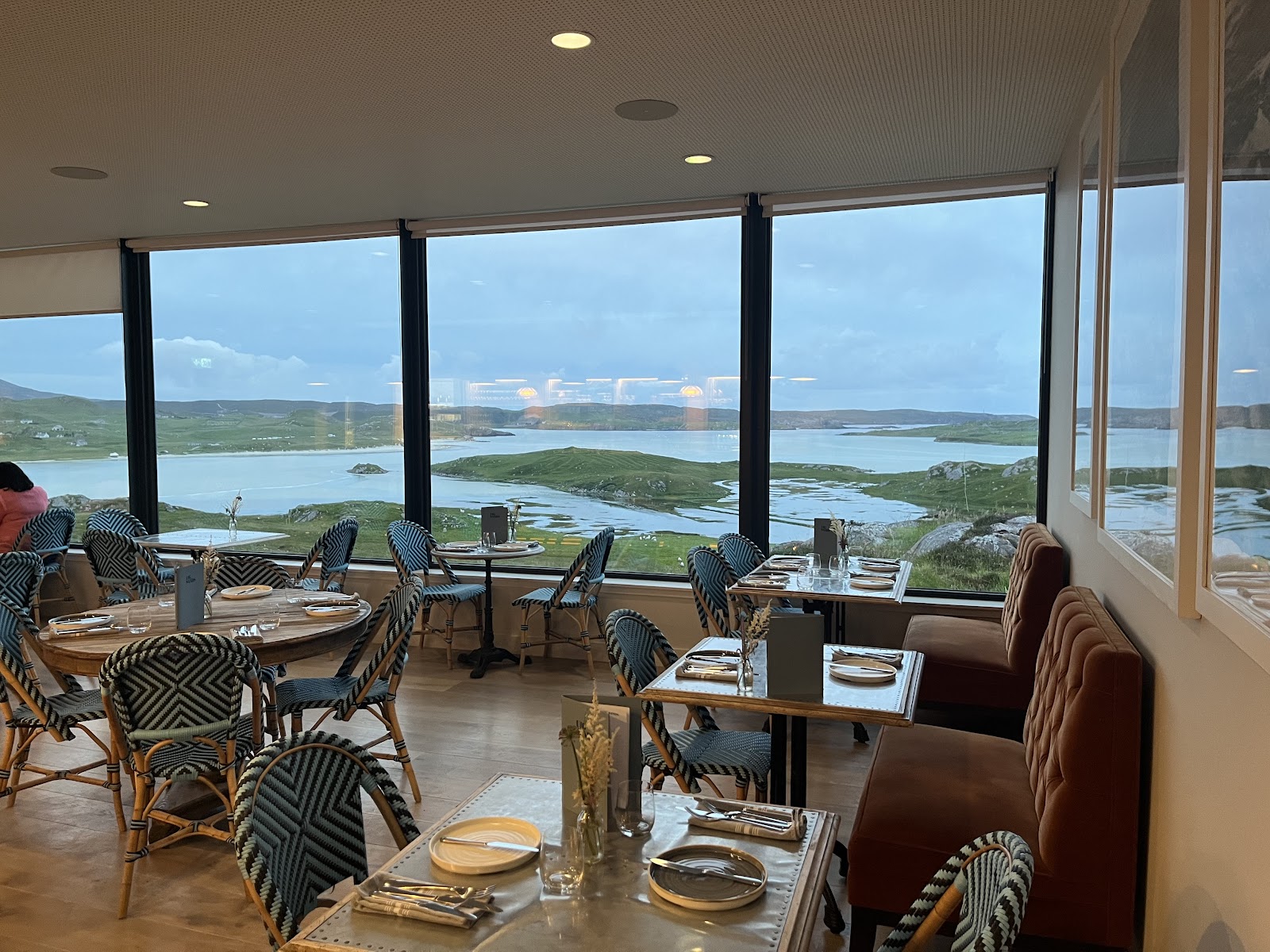 The dining room at Uig Sands Restaurant, tables and woven chairs by a wall of windows looking out over the bay and the islands of Uig.