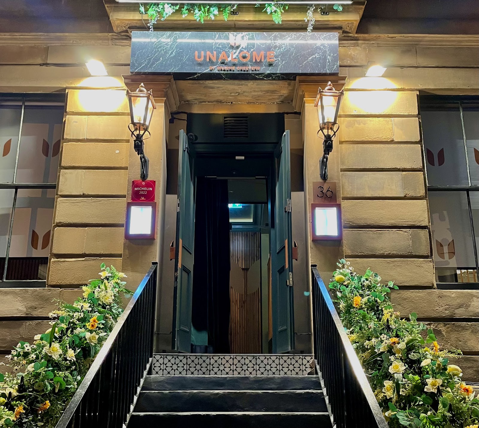The front of UNALOME by Graeme Cheevers on Kelvingrove Street at night, its marble sign above the door between two lit lanterns.