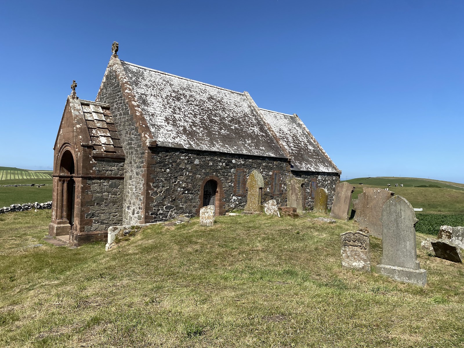 Kirkmadrine's small stone church on its rise among the fields, the red sandstone porch at its west end where the early Christian stones stand behind glass, old gravestones in the grass beside it.
