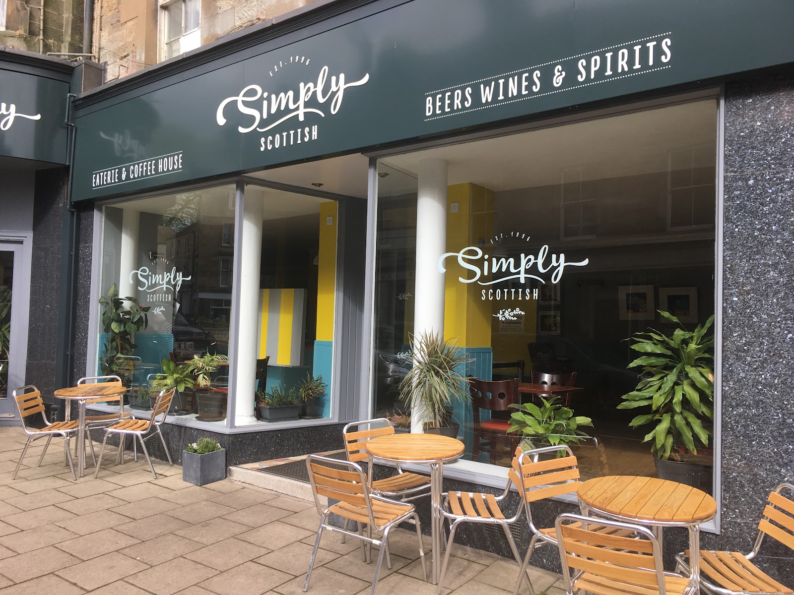 Simply Scottish on the High Street in Jedburgh, a dark grey shopfront with its name in white script and tables outside.