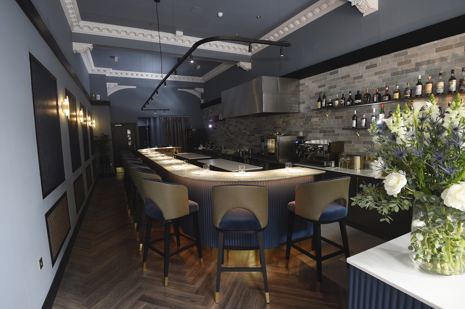 The dining counter at eòrna, a curved bar lined with upholstered stools facing the open kitchen, under a high corniced ceiling.