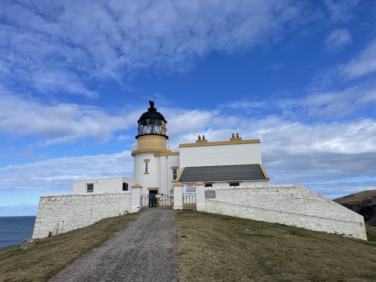 Stoer Lighthouse, a white tower and keepers' buildings against a blue sky at the end of the road.