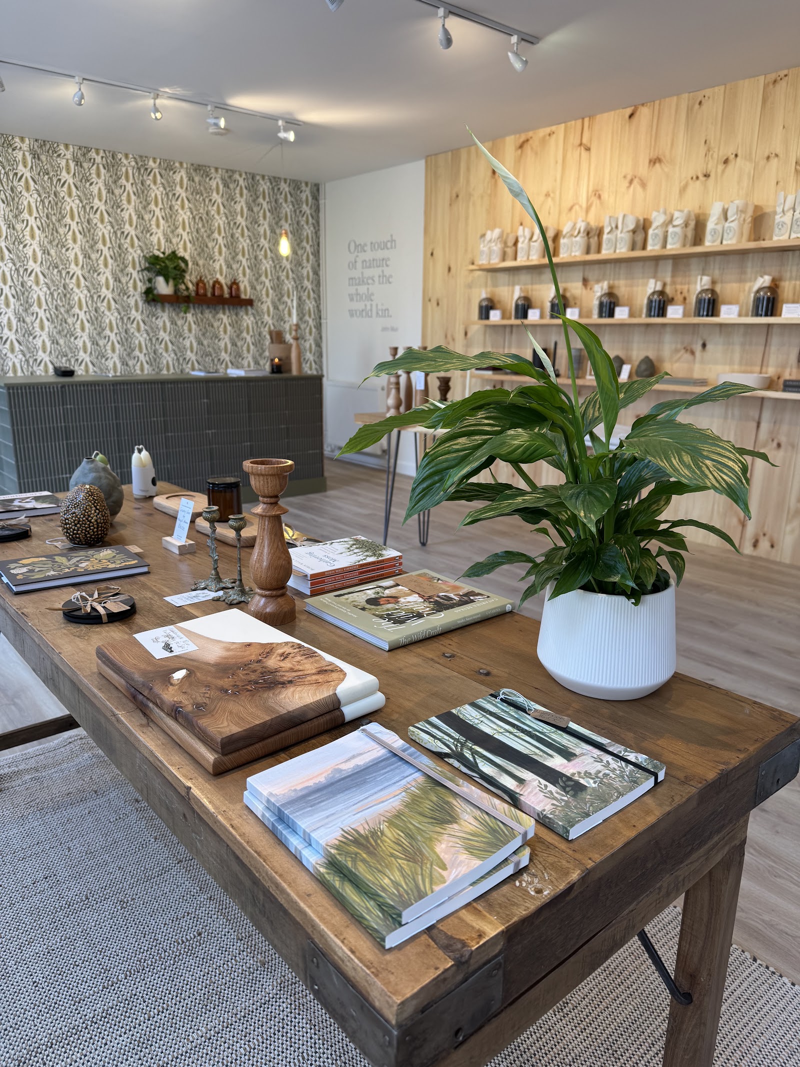 Inside SPÈ Atelier at Logie Steading, a wooden table of candles and books in a bright shop with pale wooden shelves.