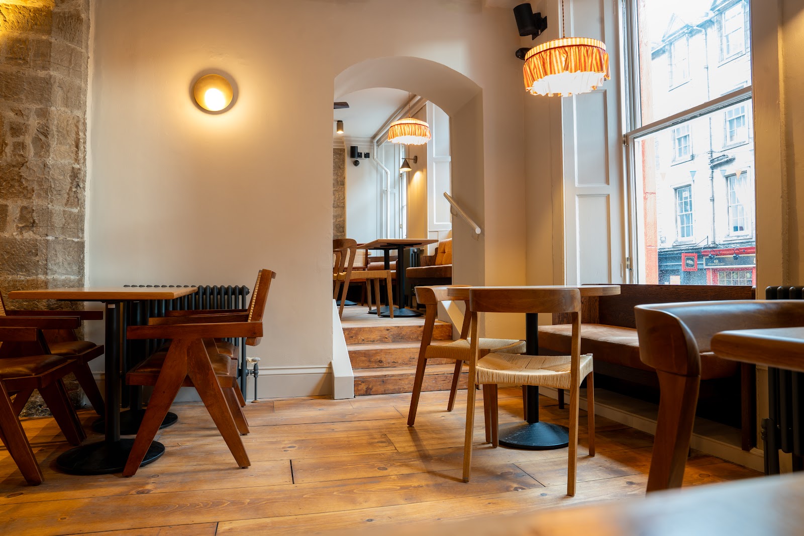Whirlybird's dining room on Victoria Street, with wooden tables and chairs, a stone wall, fringed lamps and a tall window onto the street.