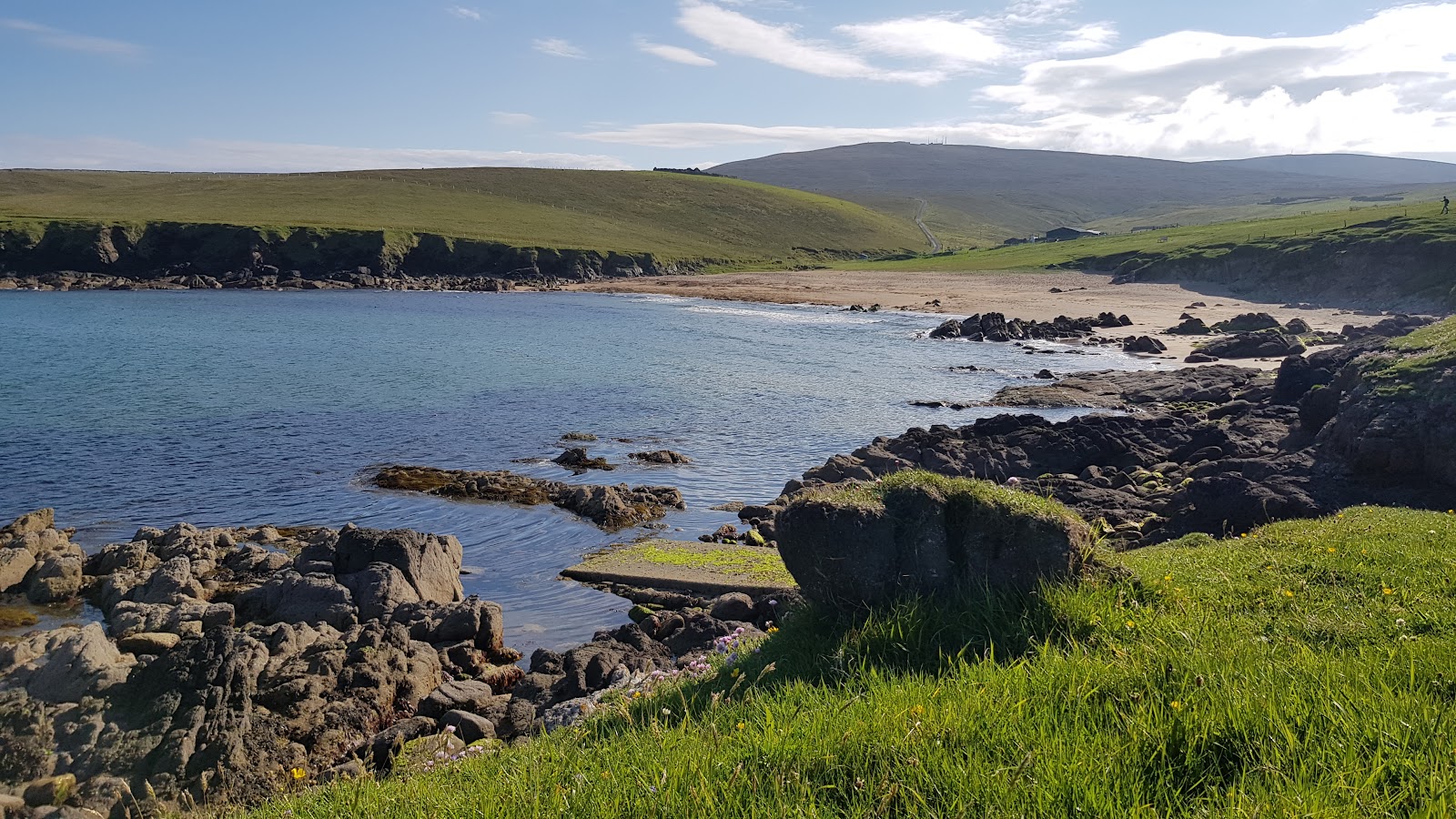 Rocks and a sandy bay on the north coast of Unst, hills behind.