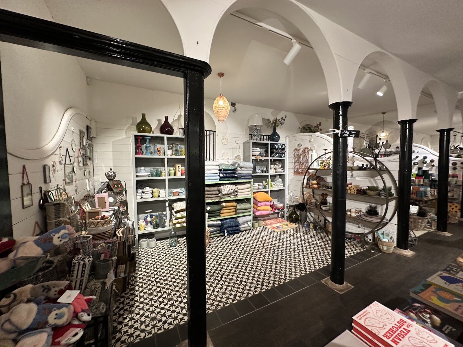 The shop inside the old stables: white arches on black iron columns, a patterned tiled floor and shelves of homeware and textiles.