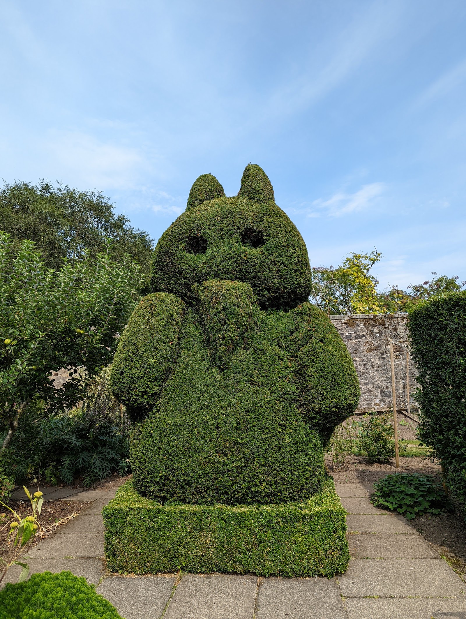 A topiary yew clipped into the shape of a seated animal on a paved square inside the walled garden.
