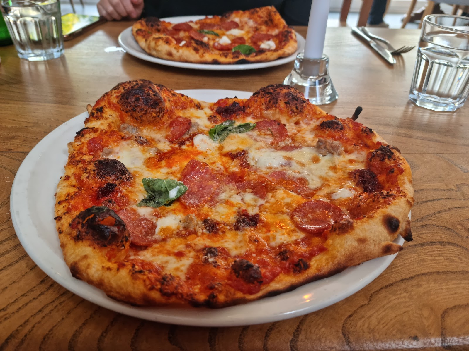 A wood-fired pizza with pepperoni, mozzarella and fresh basil on a wooden table at Nick's at Port of Menteith.