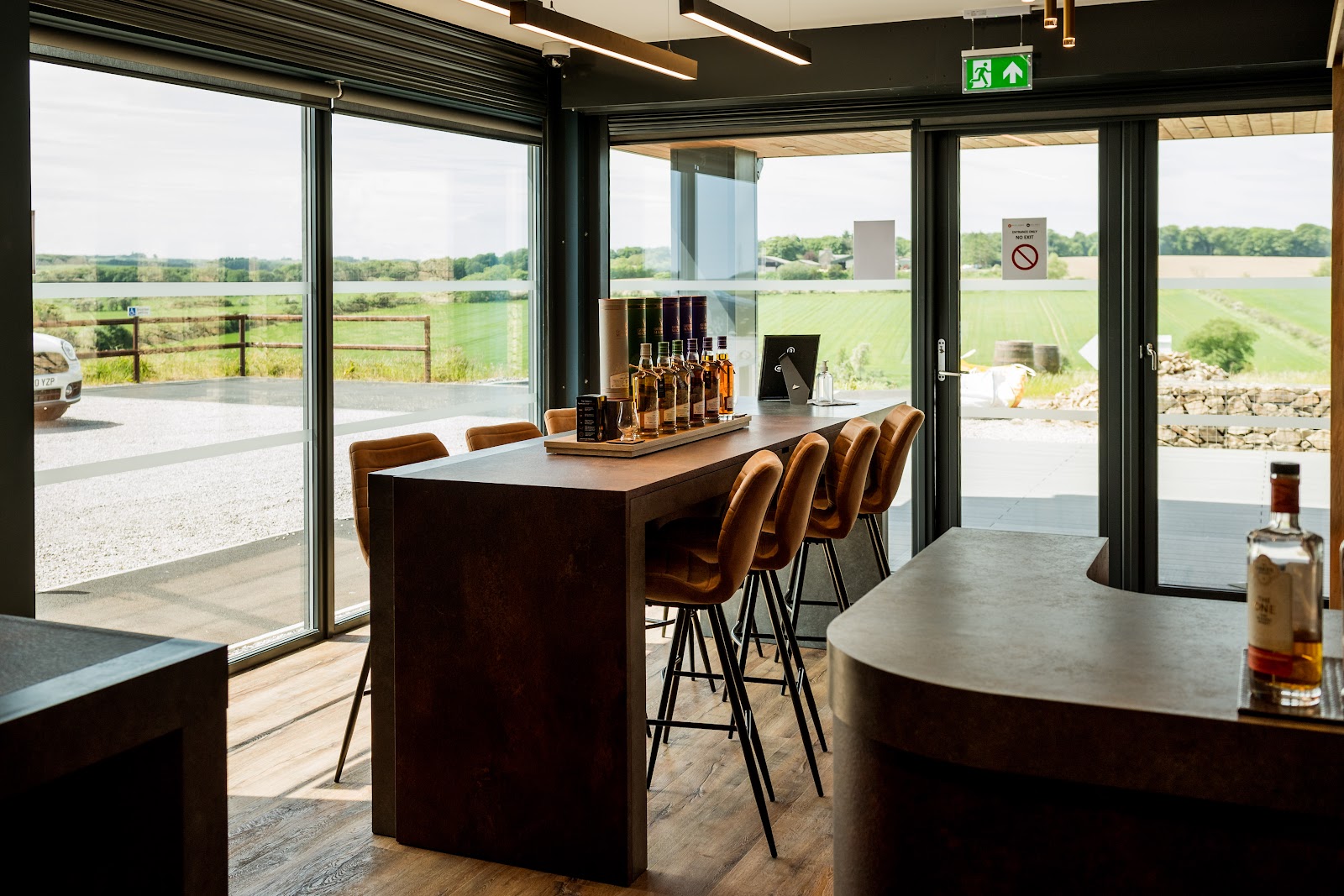 The tasting bar at Still Spirit, stools along the counter by tall windows onto the fields.