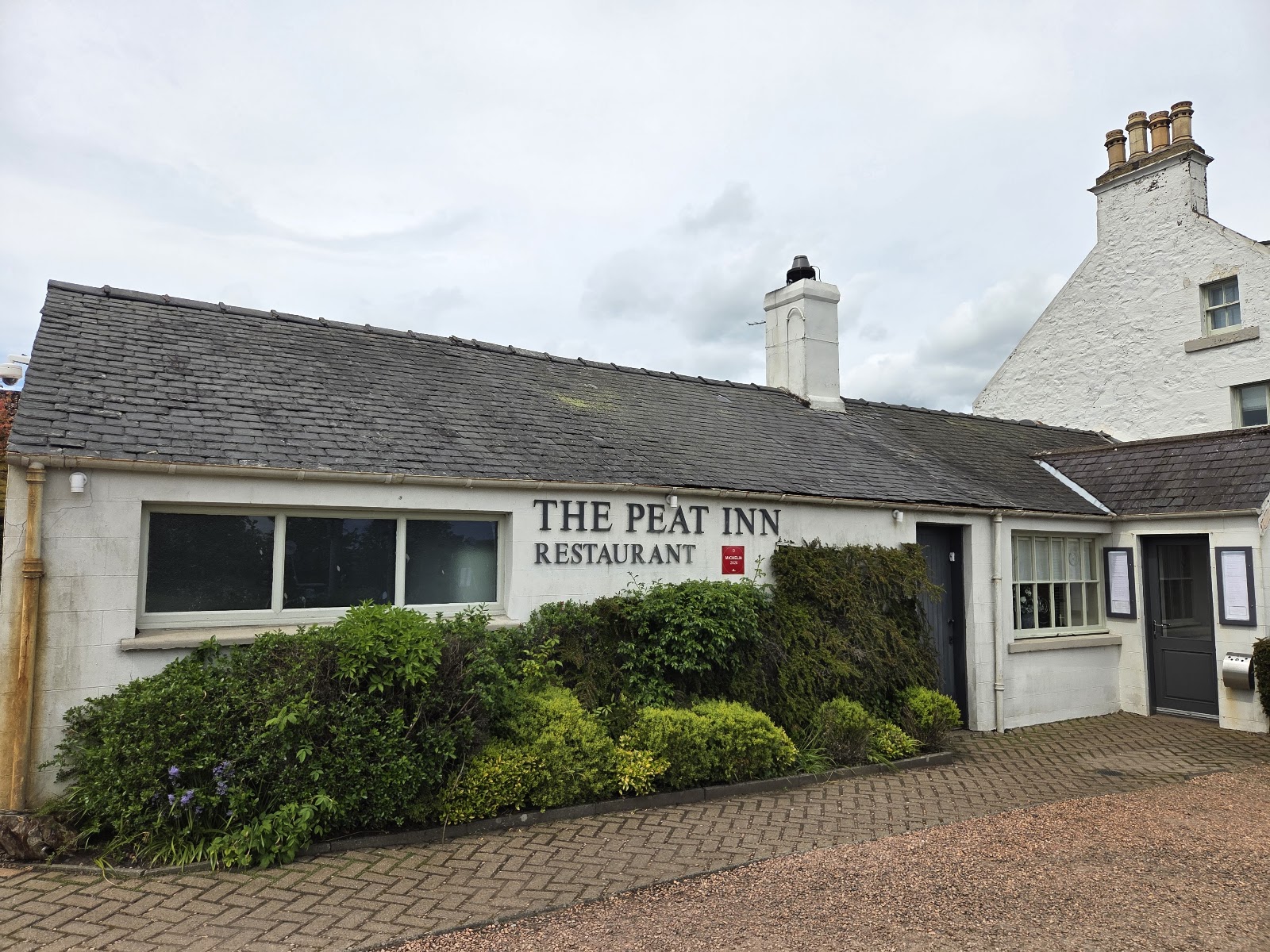 The Peat Inn, a low whitewashed inn with its restaurant sign and a green garden in front.