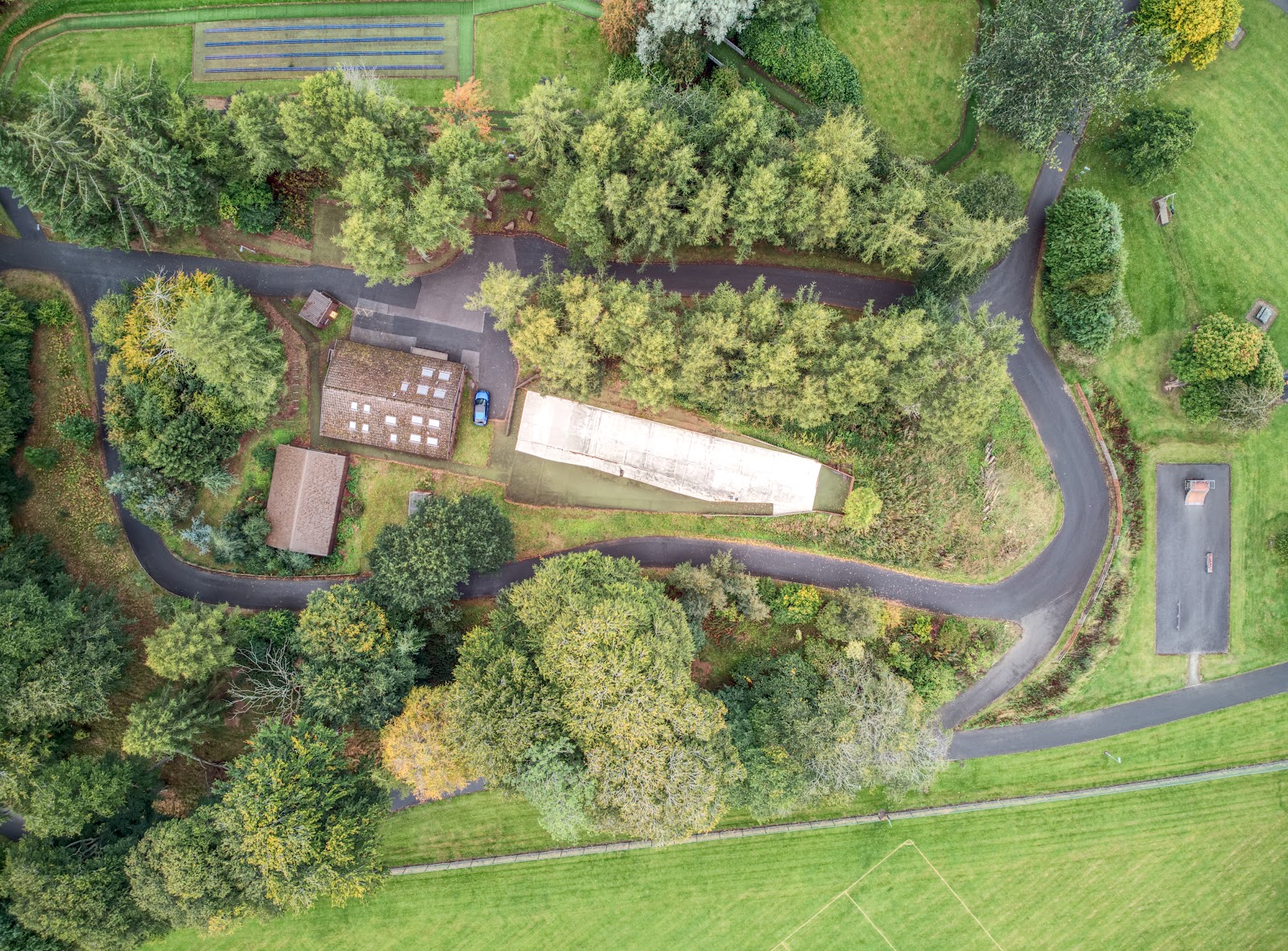 Looking straight down on the Huntly Nordic and Outdoor Centre: the lodge, the white dry slope and the loop of the roller-ski track among autumn trees, the tubing lanes at the top.
