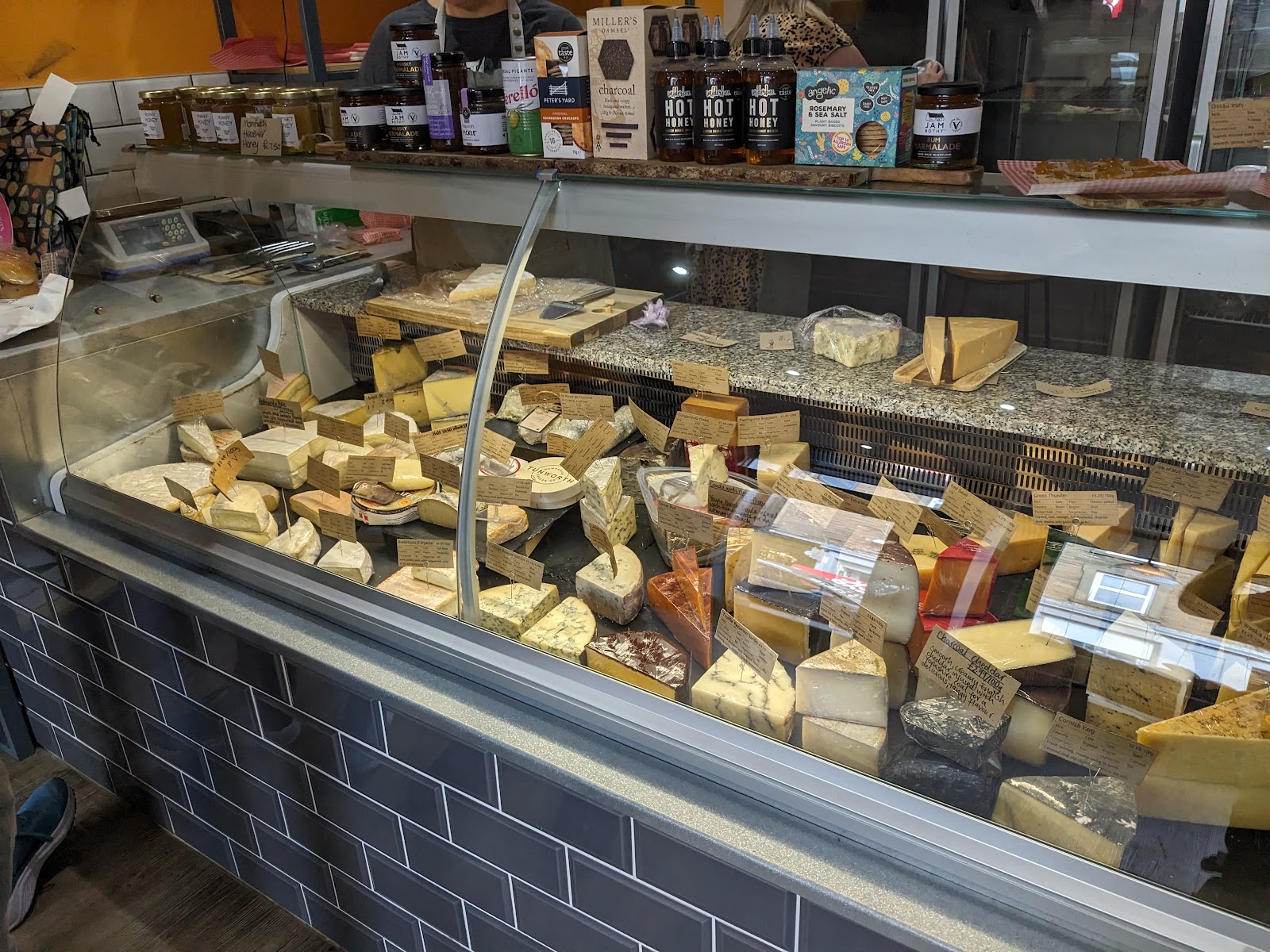 The cheese counter at The Cheesery in Dundee, full of cut wedges and whole cheeses with handwritten labels.