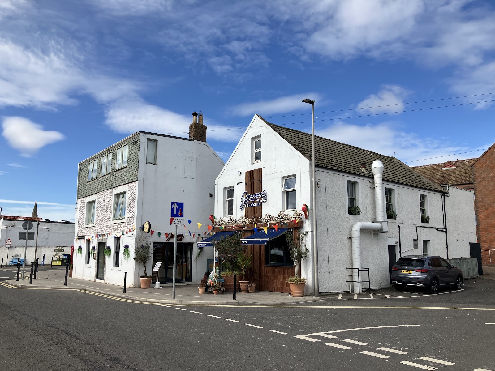 Giacopazzi's by the harbour in Eyemouth, white buildings on the harbour road with tables outside under a blue sky.