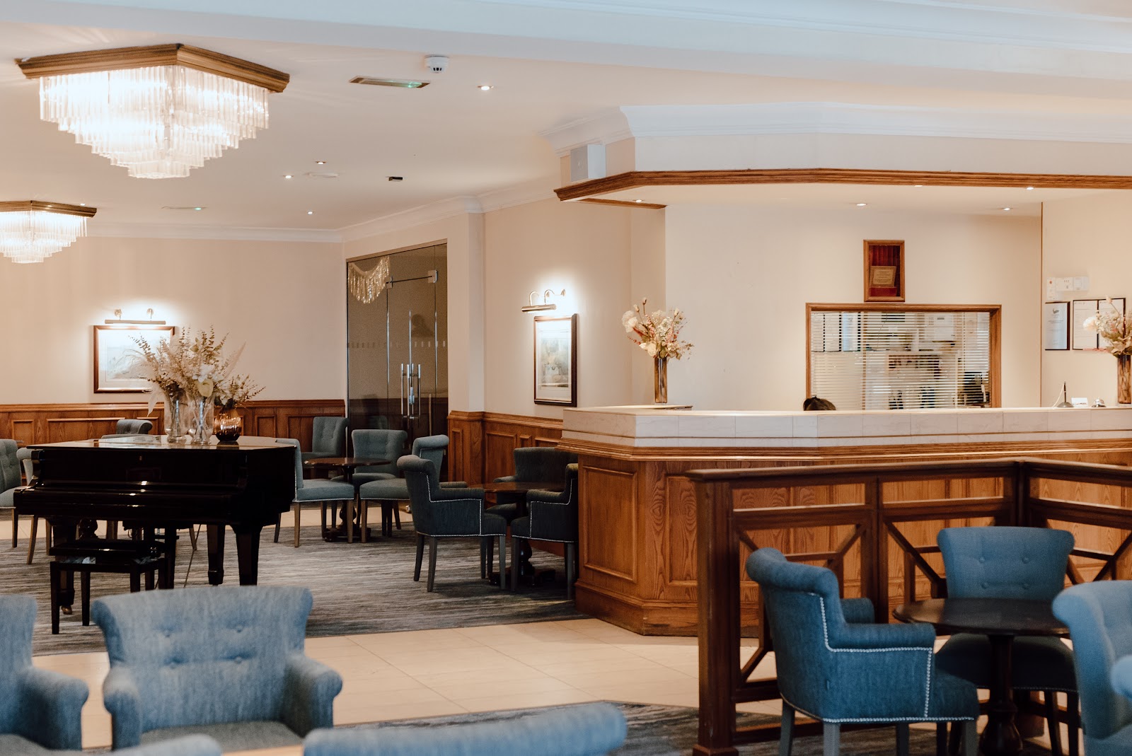 The lounge bar at the Cabarfeidh Hotel, blue armchairs round tables, a grand piano and a wooden bar under a chandelier.