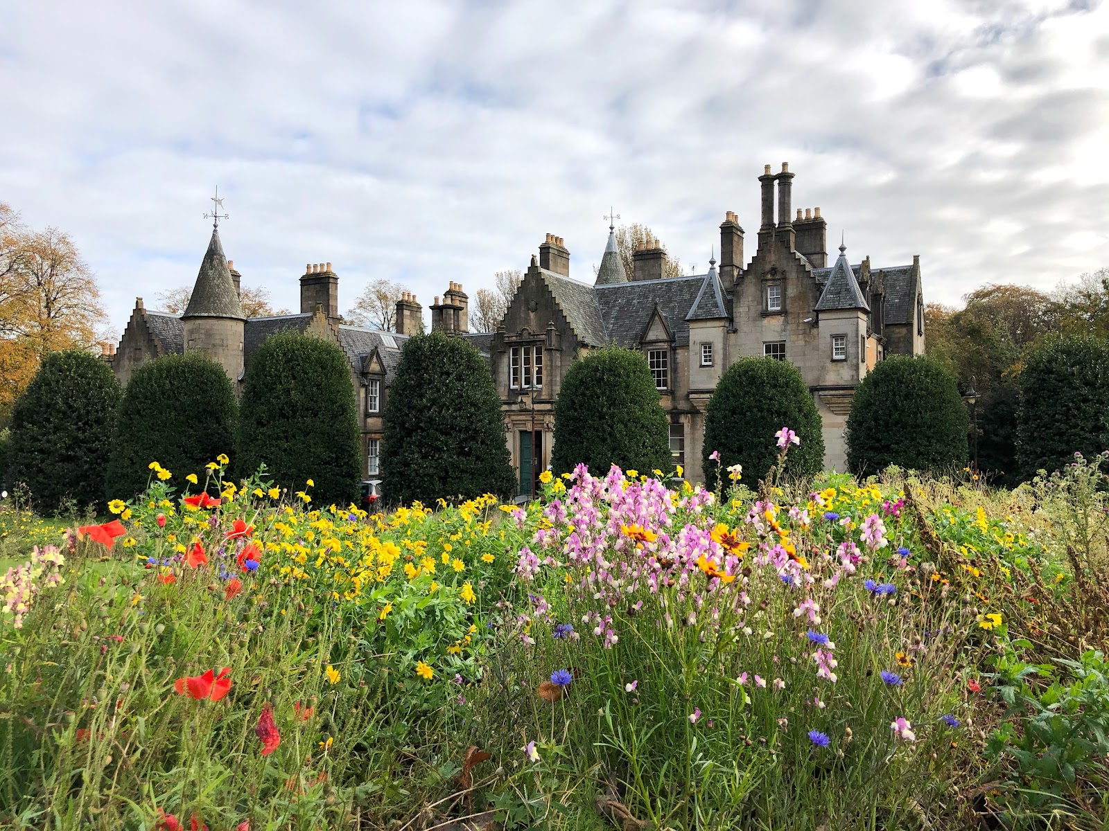 Tollcross House, a turreted baronial mansion, behind a bed of red, pink and yellow wildflowers.