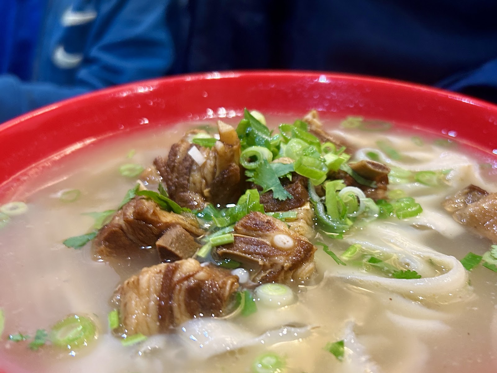 A red bowl of beef noodle soup with wide hand-pulled noodles, spring onion and coriander at Noodles and Dumplings.