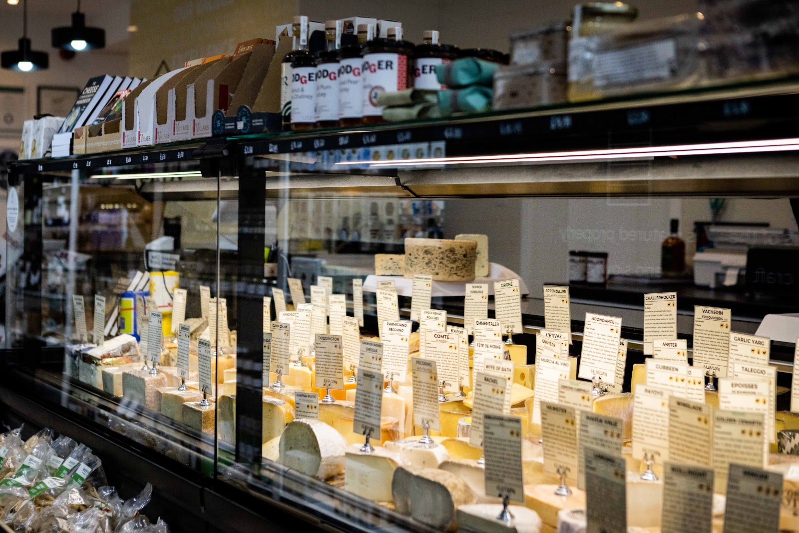 The long glass counter at The Cheese Lady in Haddington, each cheese with its own label, below shelves of bottles and jars.