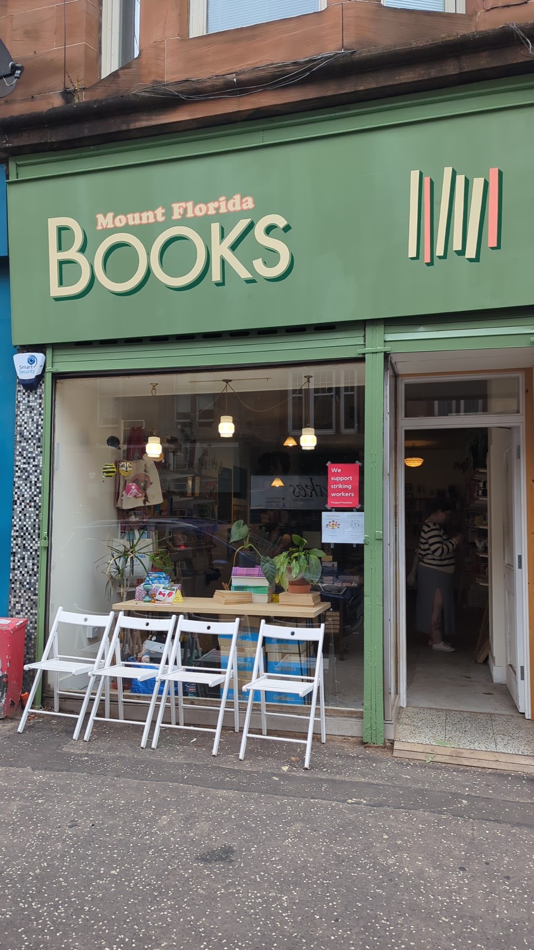 The green front of Mount Florida Books on Cathcart Road, its sign above a window of books and plants, with folding white chairs on the pavement.
