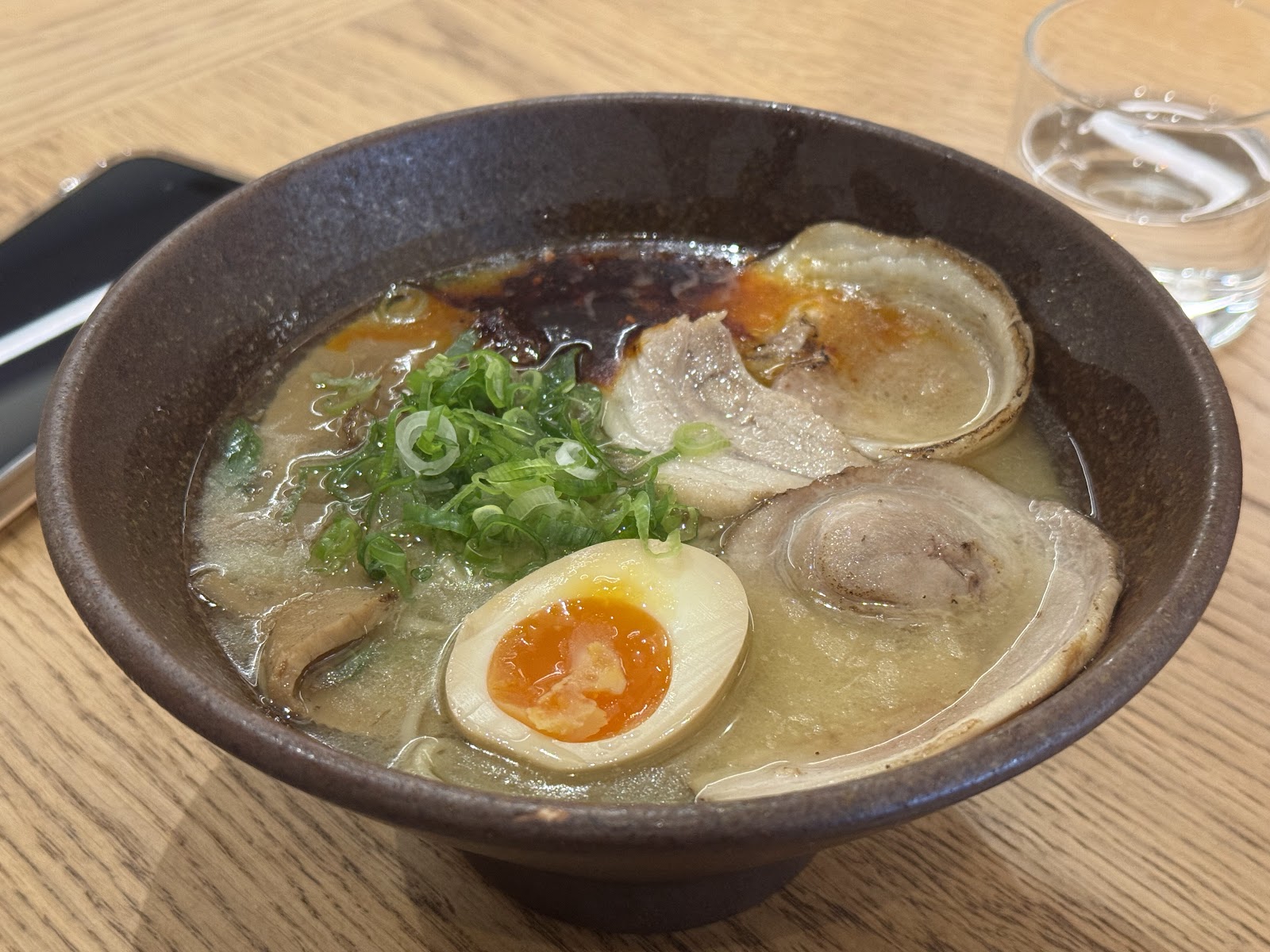 A bowl of ramen at Nishiki, with slices of chashu pork, a soft-boiled egg, spring onion and a swirl of dark oil, on a pale wooden table.