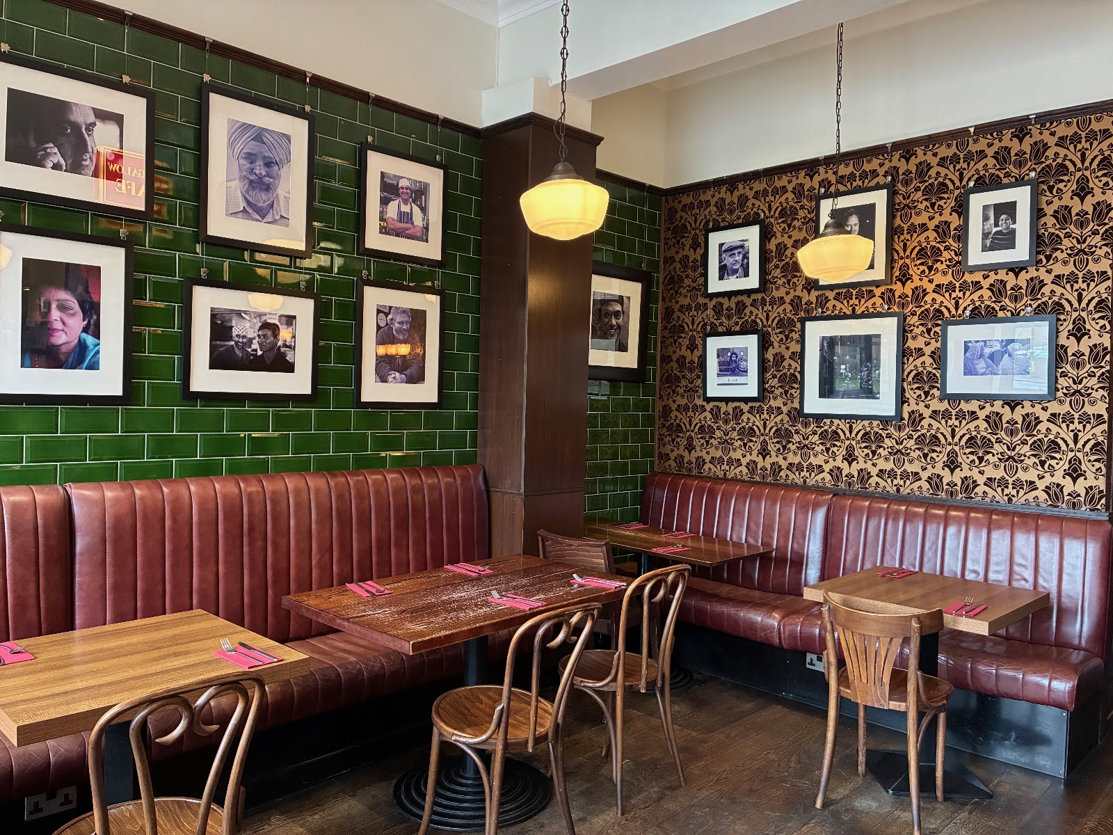 Red leather banquettes under green tiles and framed black and white portraits.