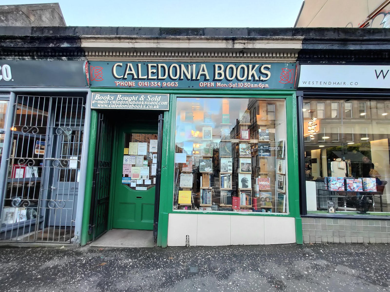 The green shopfront of Caledonia Books on Great Western Road, its painted sign over a window stacked with books and a green door papered with notices.