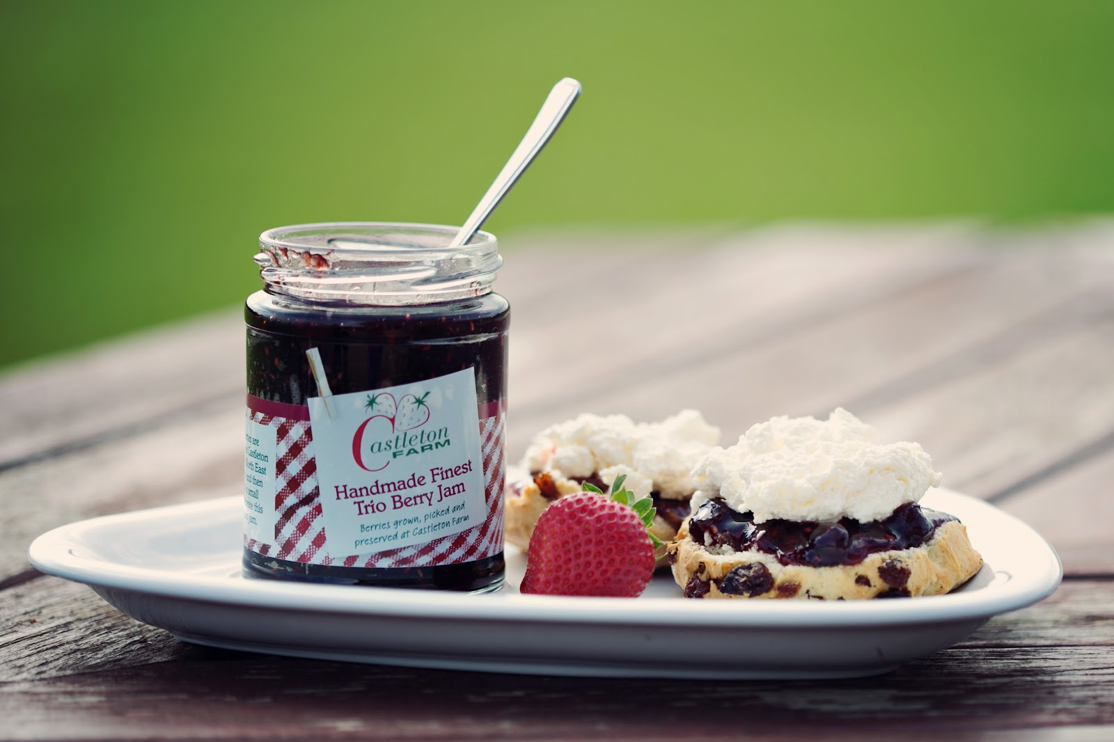 A jar of Castleton jam beside a scone with cream and berries.