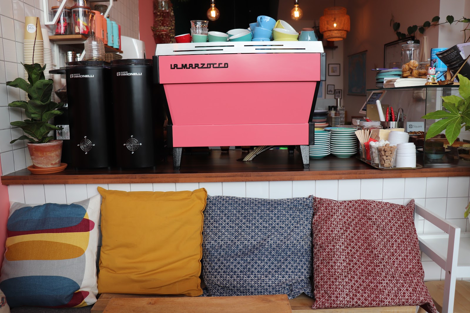 The pink espresso machine over a bench of patterned cushions.