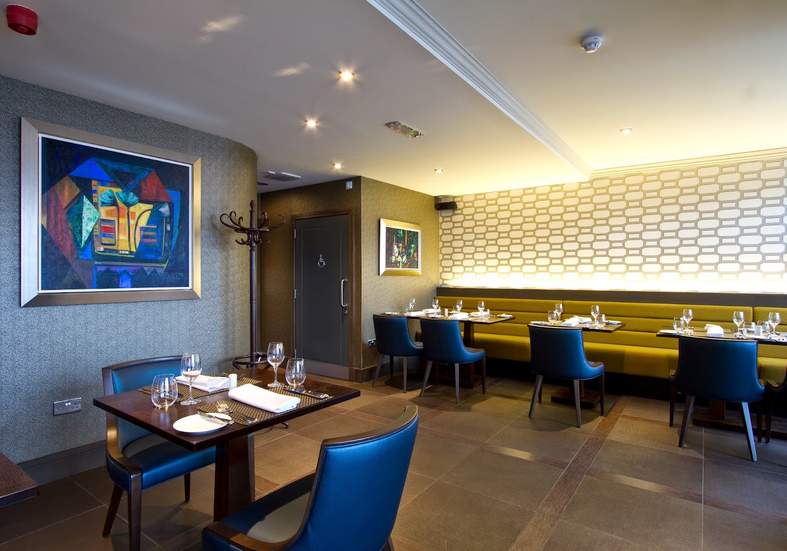 The dining room at Collinsons in Broughty Ferry, with blue leather chairs, a long mustard banquette, patterned walls and a bright modern painting.