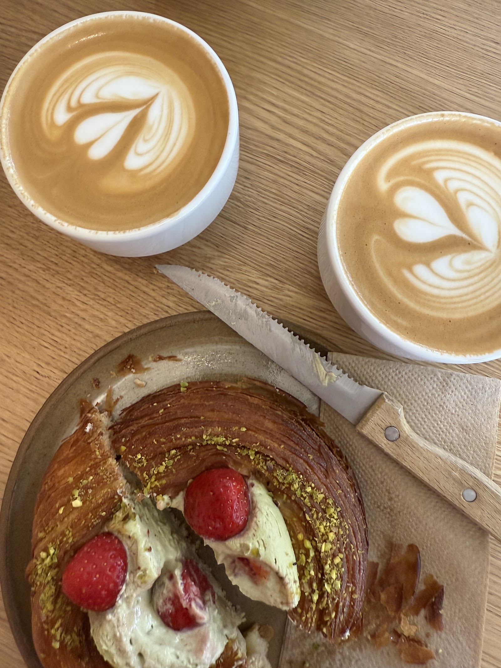 Two lattes and a pastry on a wooden table.