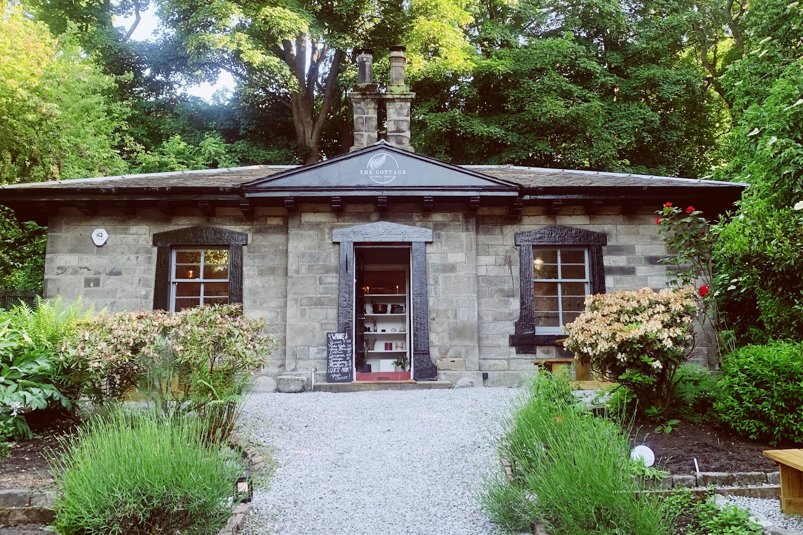 The Cottage at Royal Terrace, a low stone cottage with two chimneys among trees, a gravel path between lavender to its open door.