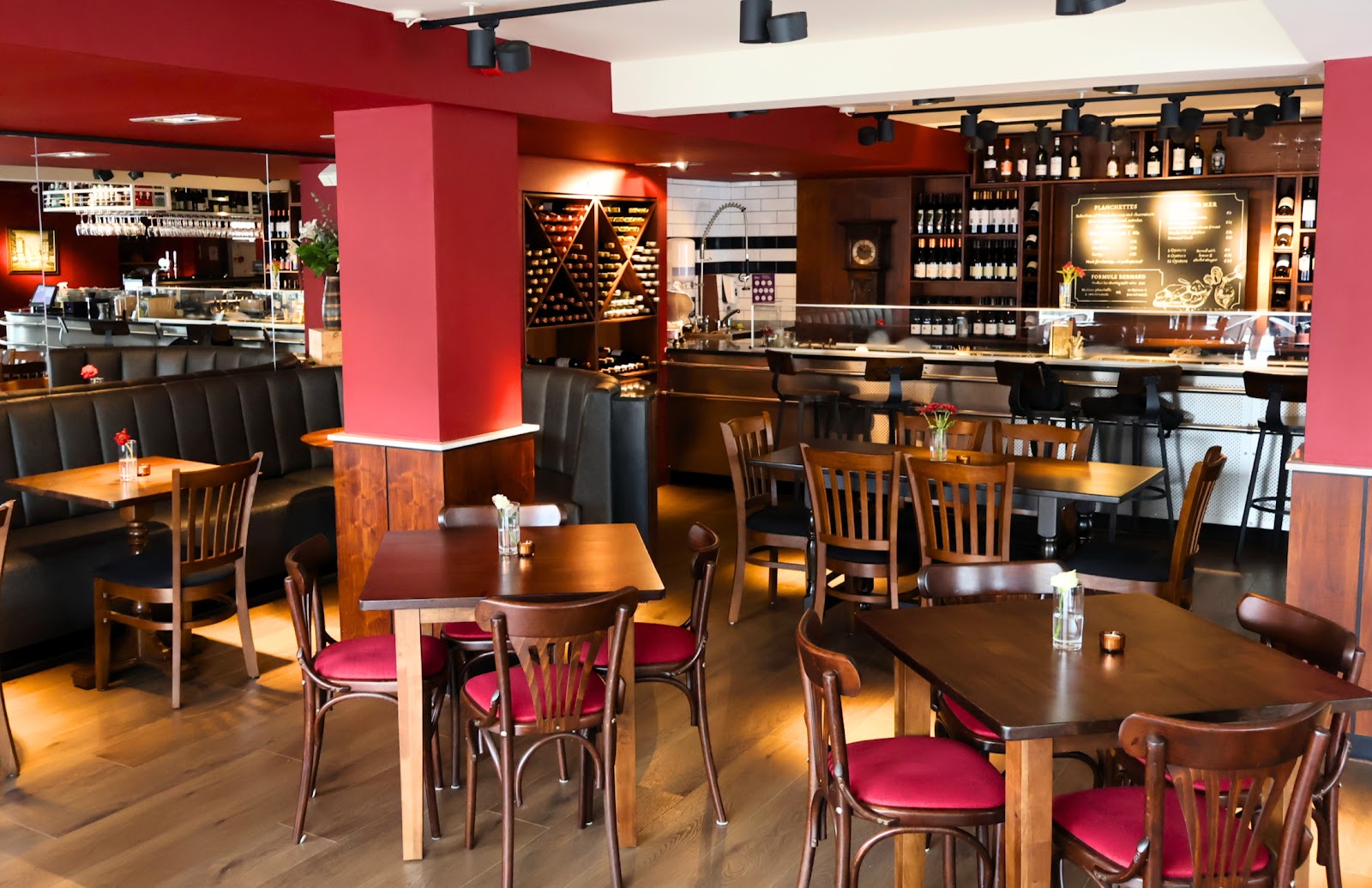 The room at Chez Bernard, with red pillars, wooden tables and chairs with red seats, and racks of wine behind the bar.