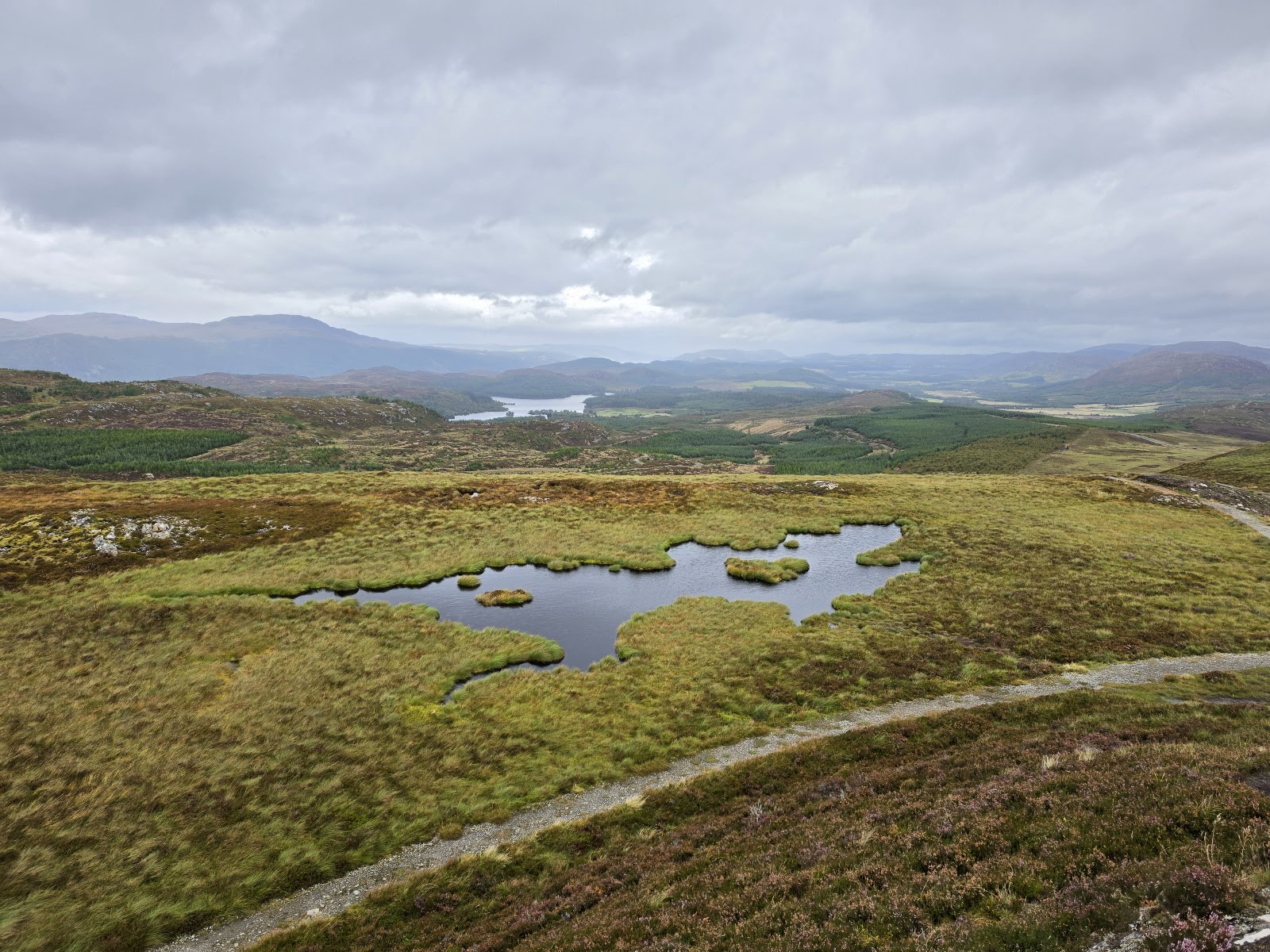 The view from Suidhe over moorland and small lochans to the hills of Stratherrick, a path curving across the heather.