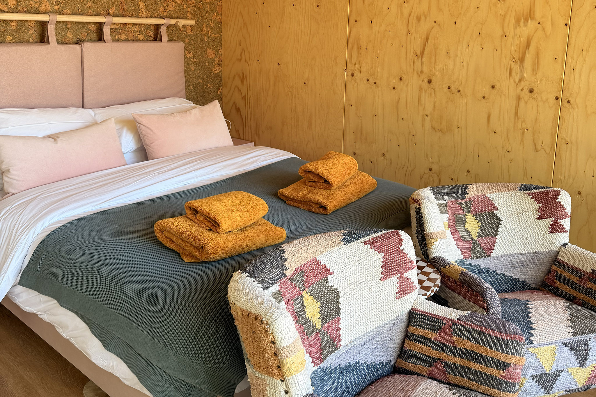 A pink leather headboard, pink and grey bedding and two patchwork armchairs in Kin's plywood room.