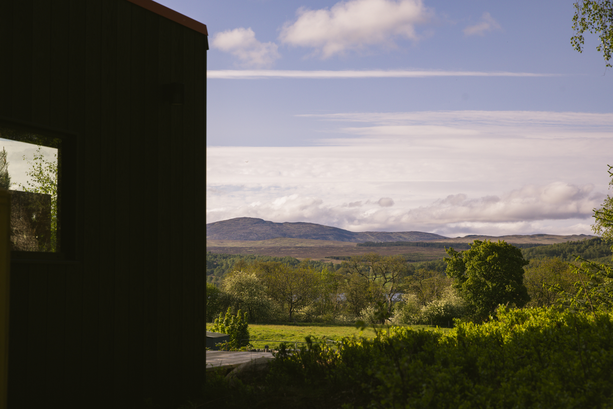 From beside Kin's black wall, a view over the fields to Loch Rannoch and the hills under a blue sky.