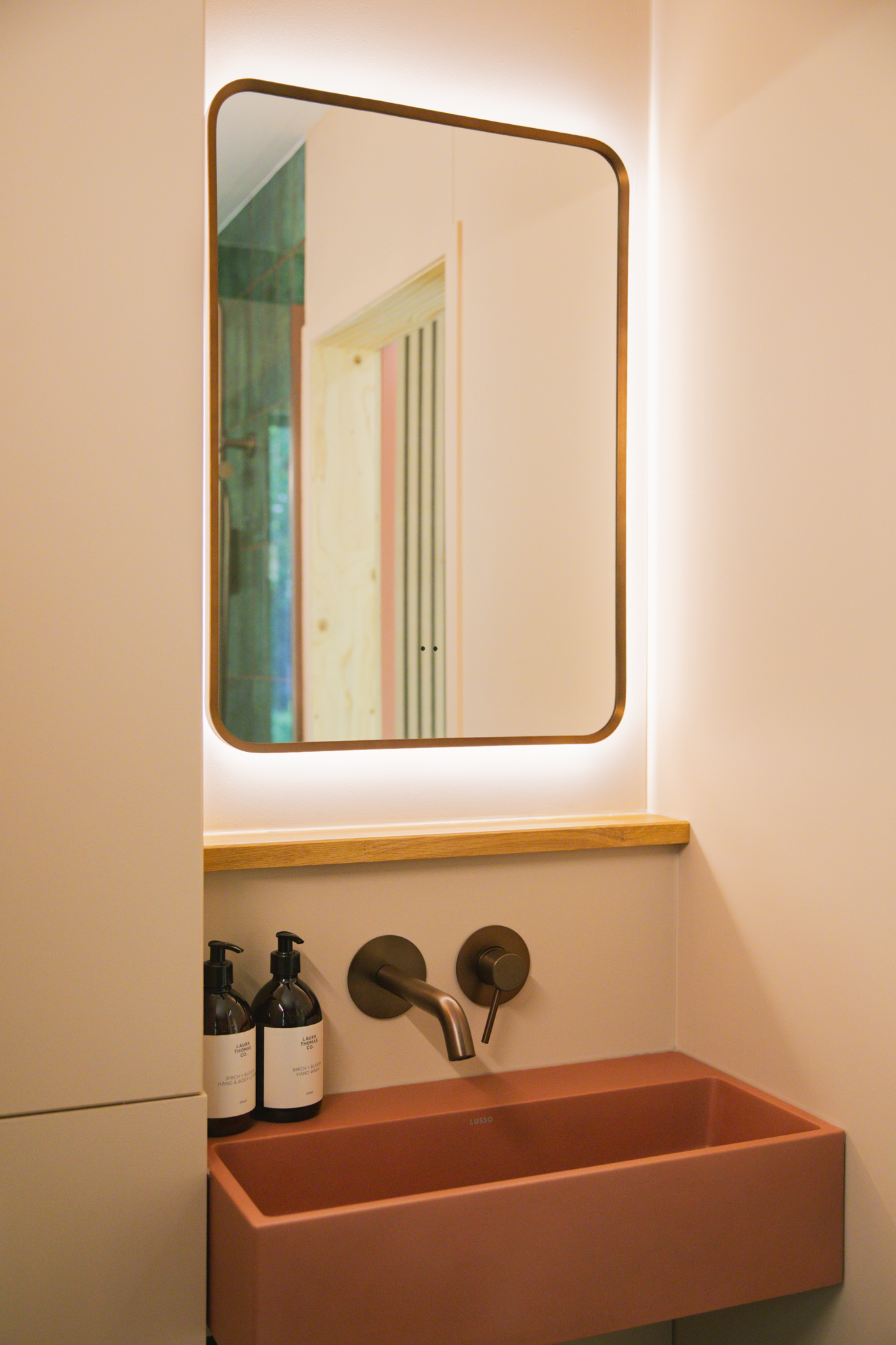 A terracotta trough basin under a round-cornered mirror lit from behind in Loch's shower room.