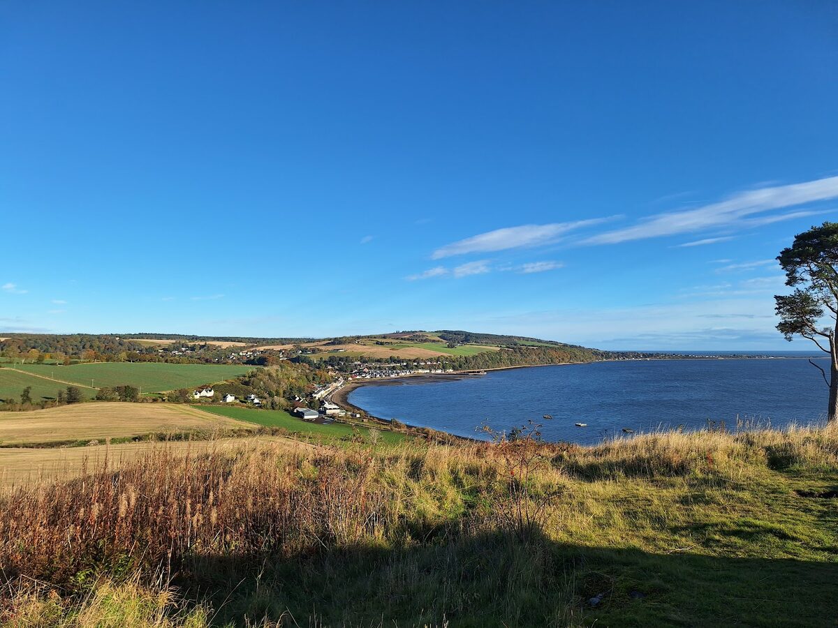 Coastal village curves along a bay, farmland rolling towards distant hills
