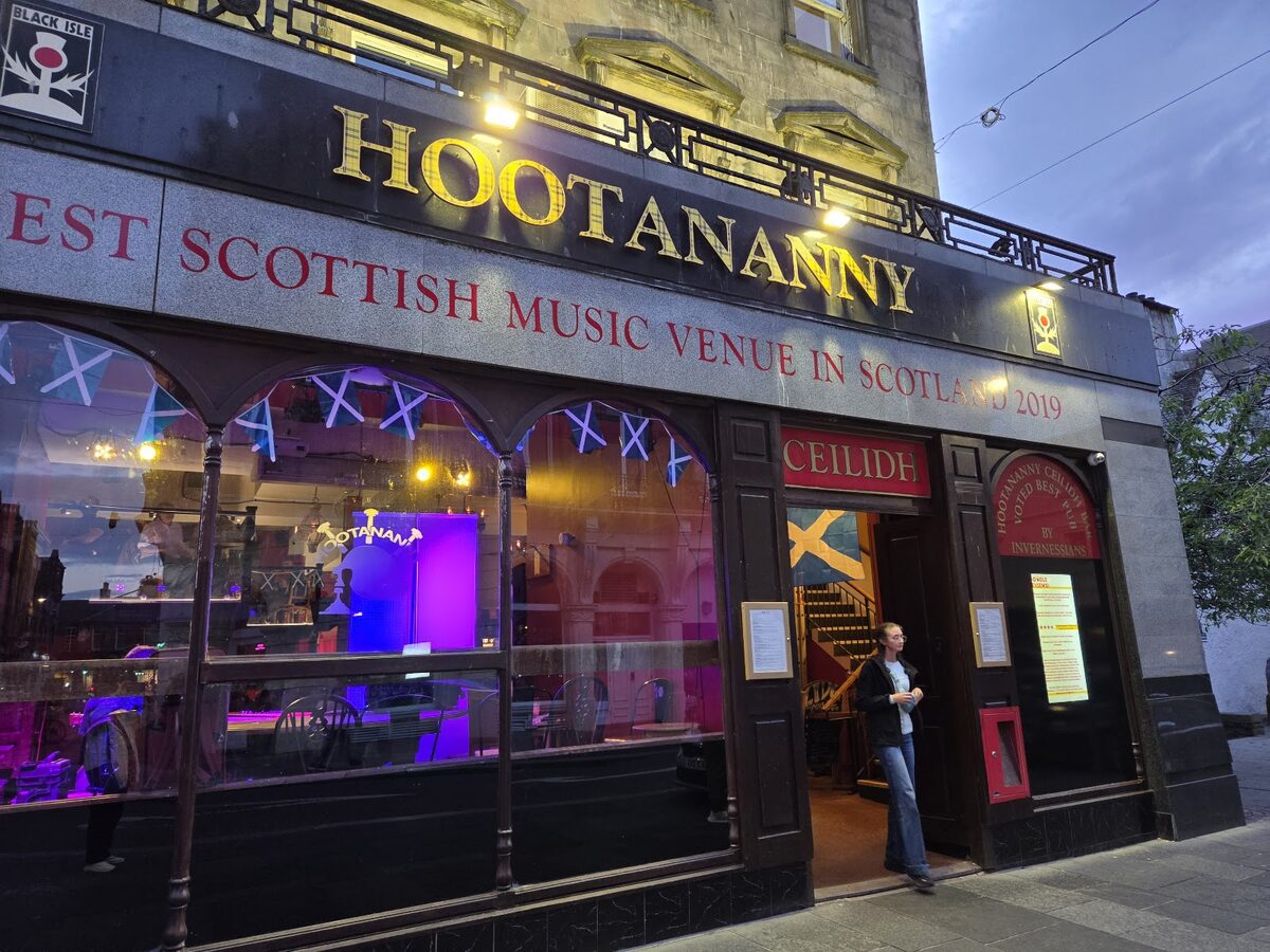 Hootananny's frontage on Church Street at dusk, gold lettering over arched windows lit purple and blue.