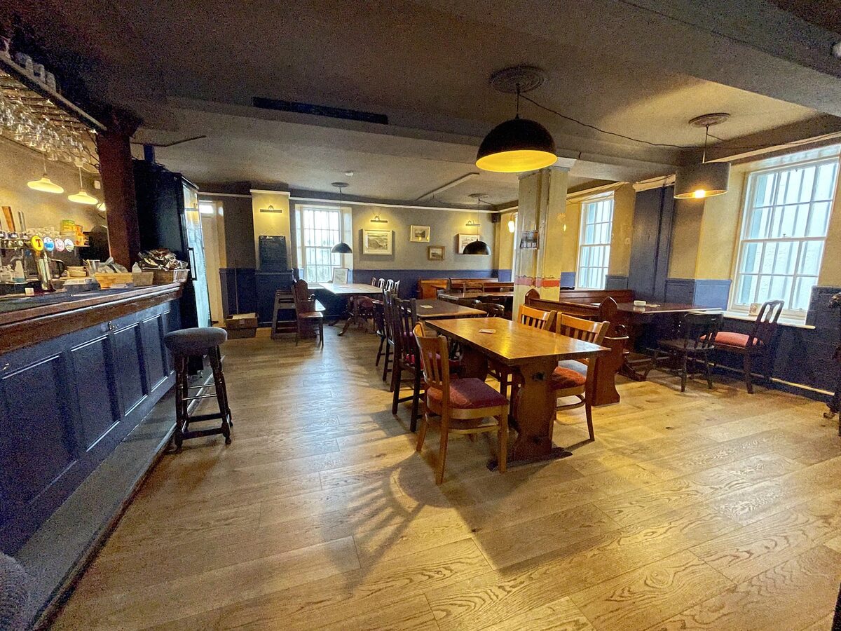 Inside the Fishertown Inn in Cromarty, a long bar of blue panelling and wooden floors with tables by the windows.