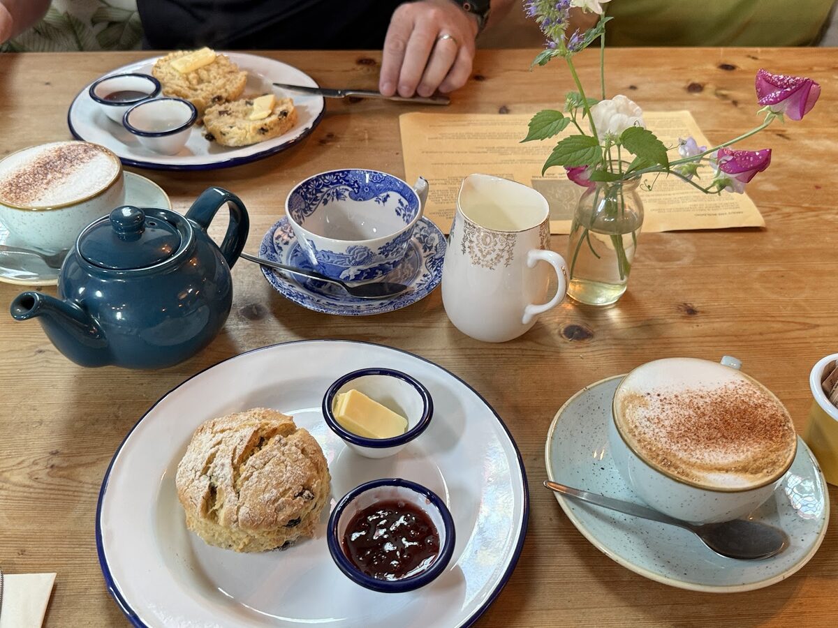 Scones with jam and butter, tea and cappuccinos on a wooden table at Artisan Cafe & Deli.