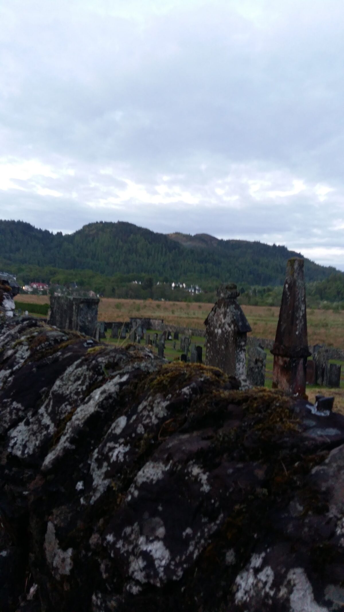 Old gravestones in the kirkyard with the hills beyond.