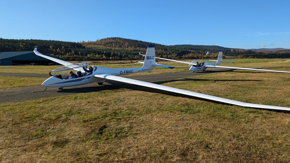 Two white gliders on the grass of Aboyne airfield, the Deeside hills beyond.