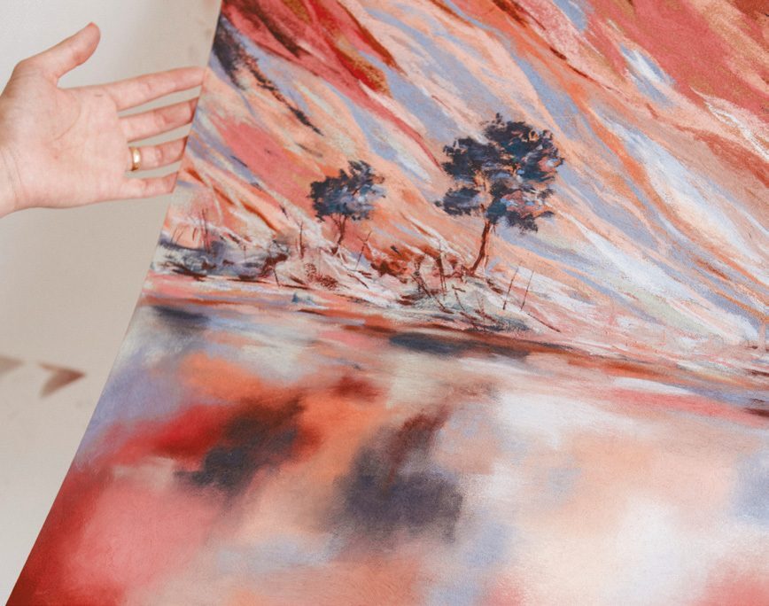 Hands holding a pastel landscape of trees and hills
