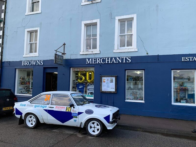 The blue front of Brown's on Tobermory's Main Street, a rally car parked outside.