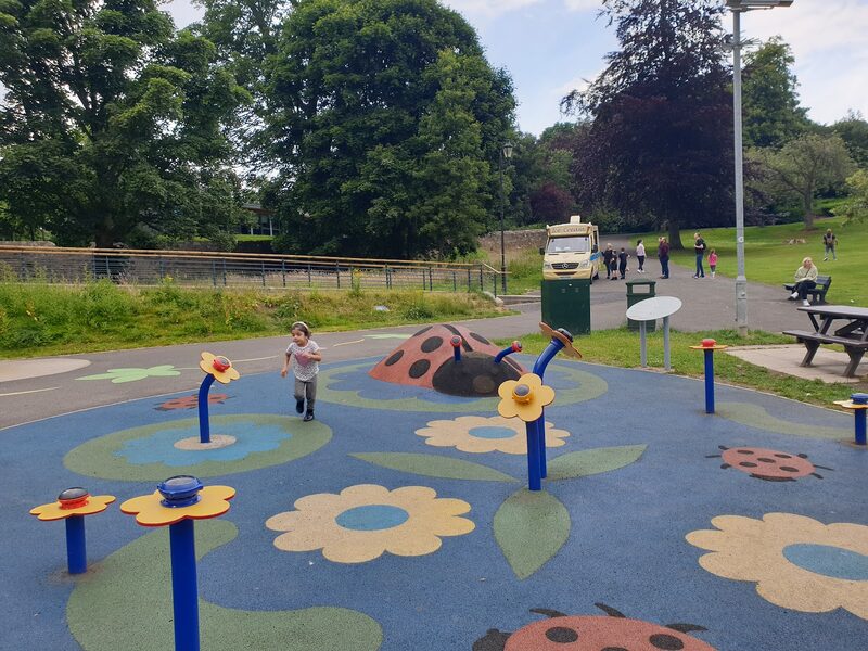 Child runs across a ladybird-themed play park, ice cream van parked behind