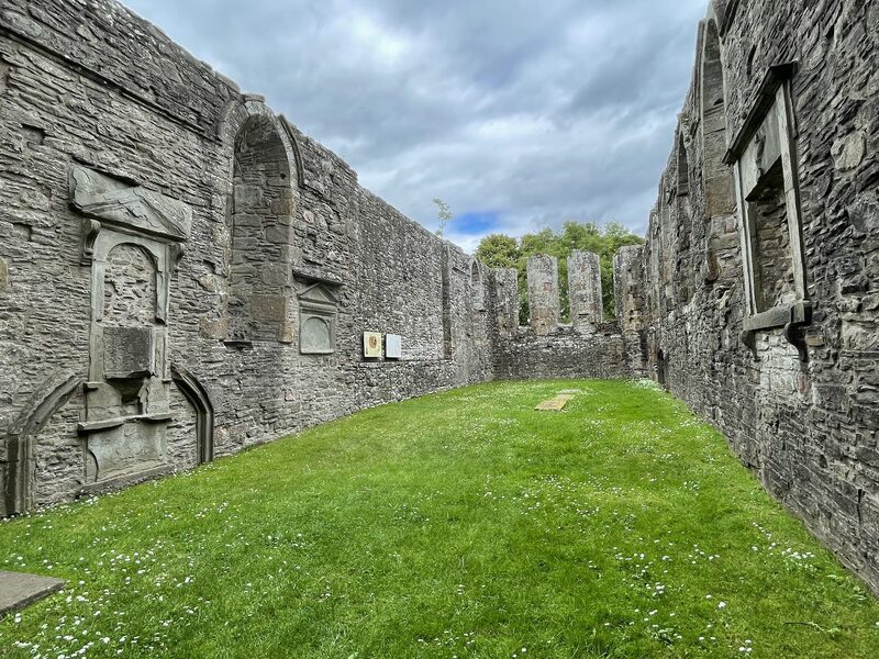 Roofless stone walls and wall tombs enclose a grassy ruined church interior