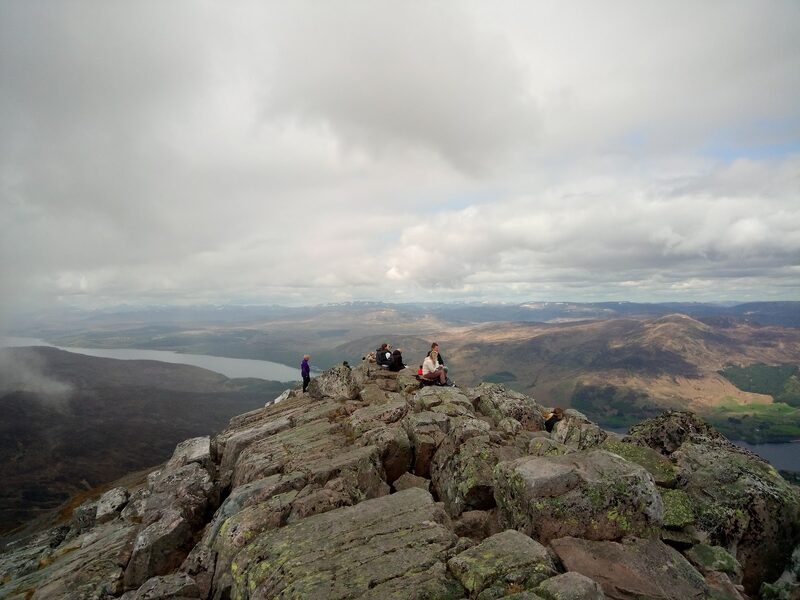 Walkers resting on the rocky summit of Schiehallion, lochs and hills far below.