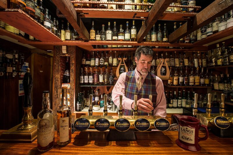 The whisky bar at The Anderson in Fortrose, a barman pulling a pint before floor-to-ceiling shelves of bottles.
